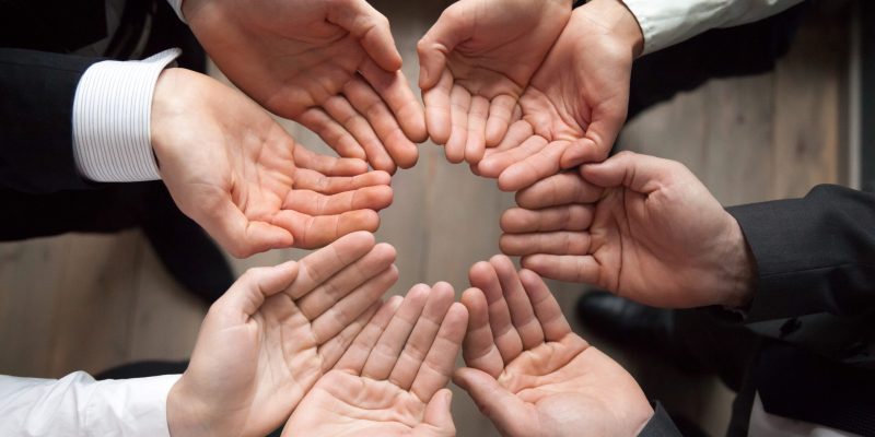 Team people join hands in circle palms up as concept of care protection, contribution in growing business and startup growth, enganing crowdfunding, unity, trust or safety concept, close up top view